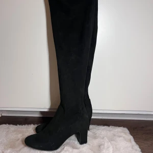Overknee mockastövlar med klack - Säljer ett par svarta, höga stövlar i mjuk mocka med rund tå och stabil klack. 7.5cm höga. Slutar över knäna. 