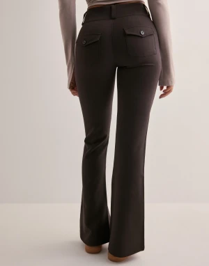 Bruna bootcut byxor med hög midja - Snygga mörkbruna bootcut-byxor med hög midja och två knappar framtill. Baktill finns fickor med lock och knappdetaljer. Byxorna har en figurnära passform upptill och vida ben nedtill, vilket ger en riktigt trendig siluett.