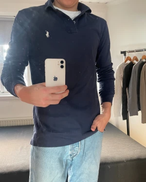 Marinblå långärmad pikétröja Polo Ralph Lauren - Snygg marinblå långärmad pikétröja från Polo Ralph Lauren med klassisk krage och två knappar. Tröjan har det ikoniska broderade polospelar-loggan i vitt på bröstet och är gjord i mjuk bomull. Storlek M. Skick 10/10 – Som Ny. Nypris ca 1200-1600 kr. ✅ Äkta vara | 📩 Öppen för frågor | 🚚 Skickas inom 24 timmar 