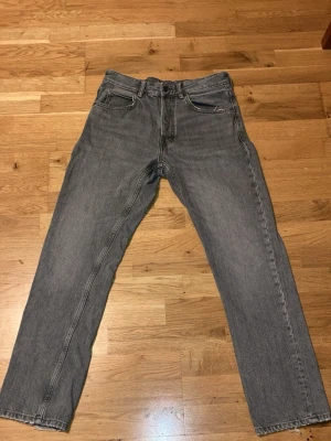 Grå raka jeans från Zara, strl 38 - Snygga grå jeans från Zara i modellen Nordics Straight. De har en rak passform och klassisk femficksdesign. Jeansen är tillverkade i ett slitstarkt bomullsmaterial och har en neutral grå färg som är lätt att matcha med olika stilar.