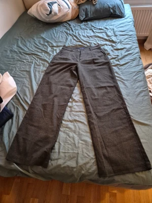 Grå kostymbyxor med wide fit - Snygga grå kostymbyxor med klassisk wide fit och hög midja. Byxorna har pressveck, bälteshällor. Materialet är mjukt och känns som ullblandning, perfekt för en clean och stilren look.