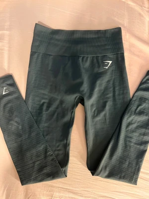 Mörkgröna seamless leggings från Gymshark - Säljer ett par helt oanvända mörkgröna seamless leggings från Gymshark med hög midja och tight passform. De har diskret struktur i tyget och logga på höften. Perfekta för gymmet eller chill hemma. Supersköna och följsamma! 