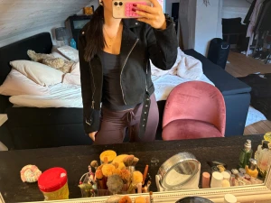 Svart mocka jacka med dragkedjor - Säljer en svart  mocka jacka med silvriga dragkedjor och detaljer. Jackan har klassisk krage, bälte i midjan och långa ärmar med dragkedja vid ärmslut. 