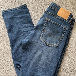 Blå jeans från Jack & Jones - Säljer ett par klassiska blå jeans från Jack & Jones i storlek 31/32. Jeansen har en rak passform med snygga kontrastsömmar och femficksdesign. Tillverkade i mjukt denimtyg som sitter skönt hela dagen.