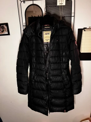 Tommy Hilfiger - Puffer jacket - En lite längre pufferjacka (går ned till knäna på mig som är 1,60) i strl S/36. Den är i mycket fint skick & har inga skavanker som tex lösa trådar, hål eller annat. Jag kommer tyvärr inte ihåg vilken modell det är & den finns ej att köpa längre. Har kontaktat deras kundtjänst & bett dem hjälpa mig att få fram vilken modell det är, så jag kommer uppdatera så fort jag fått svar från dem.