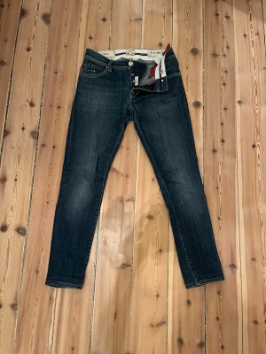 Mörkblå jeansbyxor från Tramarossa - Snygga mörkblå jeansbyxor från Tramarossa med slim passform och klassisk femficksdesign. Jeansen har röda detaljer på fickorna och insidan, samt vita kontrastsömmar. Tillverkade i mjukt denimtyg med knappgylf och diskret tvättad look.