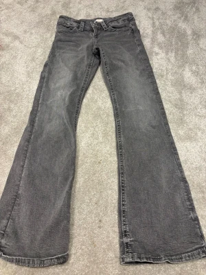 Grå bootcut jeans från Gina Tricot - Snygga grå jeans från Gina Tricot i storlek 152. Modellen har bootcut-ben och coola detaljer med flätade sömmar på bakfickorna samt silverfärgade knappar. Jeansen har klassisk femficksdesign och är tillverkade i mjukt denimtyg.