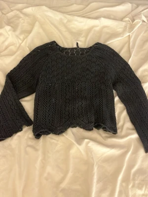 Svart stickad croppad tröja - Säljer en svart stickad tröja med lite 3 kvarts ärm och hålmönster. Tröjan är med vågig nederkant. Använd 2 gng