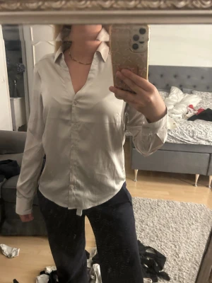 beige klassisk skjorta med knappar - Snygg beige skjorta med klassisk krage och knappar hela vägen framtill. Skjortan har lång ärm och en stilren, lite loose passform. Materialet ser ut att vara mjukt och har en lätt glans, vilket ger en fräsch och clean look. Perfekt för dig som gillar enkel och tidlös stil.