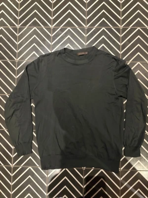 Grön tröja från Oscar Jacobsson - En stilren grön tröja från Oscar Jacobsson med rund hals och ribbade muddar vid ärmslut och nederkant. Tröjan är långärmad och har en klassisk, enkel design som funkar till många olika looks. Materialet är mjukt och känns skönt mot huden.