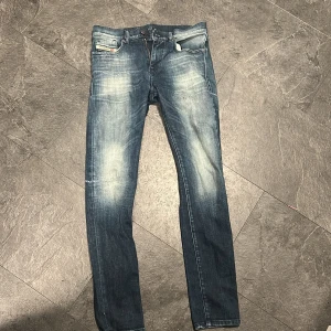 Blå Diesel Belther jeans  - Snygga blå Diesel Belther jeans med slim passform och slitna detaljer. Jeansen har klassisk femficksdesign, låg midja och coola faded effekter framtill och baktill. Röd Diesel-logga på bakfickan ger extra edge. Perfekt för dig som gillar streetstyle.