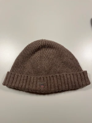 Mössa från Gant - Mössa från Gant i brun/beige med lös passform. Bra skick men använd.