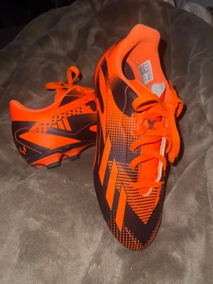 Adidas orange fotbollsskor stl 38⅔ - Säljer ett par riktigt snygga fotbollsskor från Adidas i en skarp orange färg med svarta grafiska detaljer. Skorna har snörning och mönstrad sula för bra grepp på planen. Tillverkade i syntetmaterial och designade för att sticka ut på matchen.