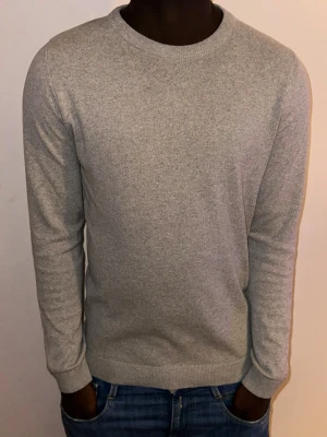 Lindbergh grå stickad tröja – Relaxed Fit, storlek S -  Snygg och stilren grå stickad tröja från Lindbergh i modellen *Relaxed Fit*. Tröjan är i storlek S och har en mjuk, behaglig kvalitet som gör den perfekt för både vardag och jobb.  Den har rund halsringning, ribbade muddar och en klassisk passform som sitter avslappnat utan att kännas för lös. Plagget är i mycket fint skick, utan synliga defekter.