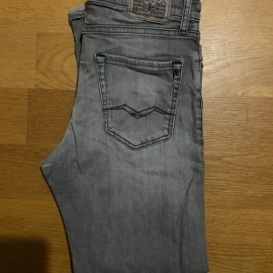 Grå jeansbyxor (Replay) - Snygga grå jeansbyxor från replay med klassiska fem fickor. Byxorna har svarta detaljer på bakfickorna och en diskret tvättad look. Perfekta för en avslappnad stil och passar till det mesta.