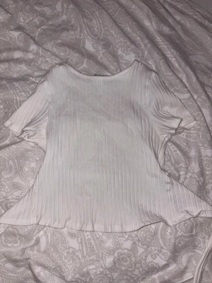 Vit ribbad topp med knyt i ryggen - Säljer en fräsch vit topp med ribbad struktur och korta ärmar. Toppen har en snygg detalj med knytning i ryggen som ger en extra touch. Materialet känns mjukt och skönt mot huden, perfekt för dig som gillar stilrena och enkla plagg.