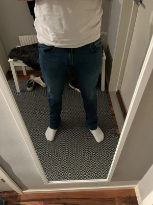 Blå Replay Anbass jeans  - Säljer ett par snygga blå Replay Anbass jeans med klassisk femficksdesign och raka ben. Jeansen har en mörk tvätt med lätt slitning och detaljerade bakfickor. Passformen är normal och materialet är stretchigt jeans för extra komfort.