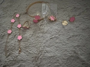 Smyckesset med rosa blommor - Säljer ett smyckesset i guldton med rosa blommor. Setet innehåller armband, ring, halsband och örhängen. Alla delar har söta blommor i ljusrosa emalj och guldfärgad metall. Perfekt för dig som vill ha en söt och färgglad accessoar till din outfit.