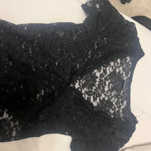 Svart spetsblus med v-ringning - Säljer en svart blus från gina med v-ringning och korta ärmar. Blusen är helt i spets med blommigt mönster och har en transparent look som ger en cool vibe. Perfekt för dig som gillar detaljer och vill sticka ut lite extra.