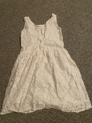 Vit spetsklänning Hampton Republic - Superfin vit kortklänning från Hampton Republic med blommigt spetsmönster och knappar baktill. Klänningen är ärmlös och har en mjuk bomullskänsla på insidan. Perfekt för sommarens alla tillfällen!