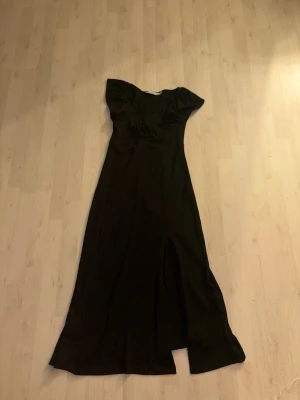 Svart långklänning med slits - Säljer en svart långklänning med korta ärmar och snygg slits framtill. Klänningen har en feminin v-ringad hals och knyt i midjan som ger en fin siluett. Perfekt för dig som gillar stilrena och eleganta plagg.