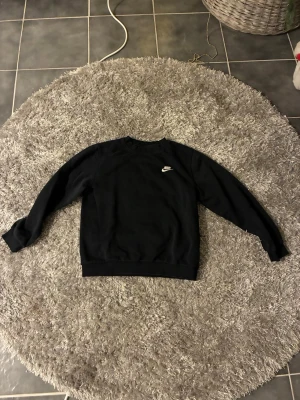 Svart Nike sweatshirt med logga - Svart sweatshirt från Nike med klassisk vit logga på bröstet. Tröjan har rund hals, långa ärmar och ribbade muddar vid ärmslut och nederkant. Perfekt för chill eller träning, enkel att matcha med jeans eller joggers. Storleken är xs eller s beroende på hur lång överkropp man har.