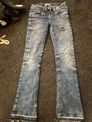 Blå bootcut jeans från LTB - Säljer ett par blå bootcut jeans från LTB med slitna detaljer och fransade benslut. Jeansen har klassisk femficksdesign, låg midja och snygga slitningar på benen. Materialet är jeans med kontrastsömmar och en cool tvättad look.