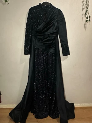 Mörkblå glittrig långklänning Giffinseti - Pris kan diskuteras säljer en mörkblå långklänning från Giffinseti i storlek M. Klänningen har glittrig överdel med långärmade partier och hög krage, samt ett svepande satintyg i kjolen. Asymmetrisk omlott-detalj framtill och dragkedja i ryggen. Perfekt för dig som vill sticka ut.