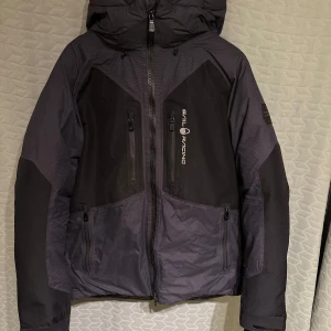 Svart dunjacka från Sail Racing limited edition  - Säljer en svart dunjacka från Sail Racing med huva och flera dragkedjeförsedda fickor. Jackan har quiltad insida med 800 fill power dun och snygg Sail Racing-logga på bröstet. Perfekt för kalla dagar och har en sportig look.