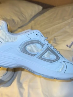 Vita CP Company sneakers med mesh - Säljer ett par fräscha vita sneakers från CP Company med silvriga detaljer och logga på hälen. Skorna har en rund tå, platt sula och snörning. Ovandelen är i mesh och syntet vilket ger en sportig vibe. Perfekta för dig som gillar stilrena och moderna sneakers.