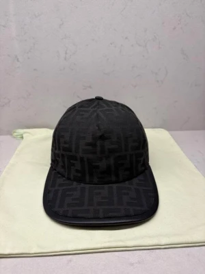 Svart Fendi keps - Säljer en svart keps från Fendi med det klassiska FF-monogrammet över hela kepsen. Kepsen har böjd skärm och är tillverkad i ett slitstarkt tyg med snygg struktur. Perfekt accessoar för dig som vill ha en lyxig och stilren look.äkta