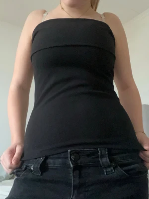 Svart tubtopp med dragkedja - Säljer en svart tubtopp med en snygg silverfärgad dragkedja längs sidan. Toppen är tight och axelbandslös, perfekt för dig som gillar minimalistisk stil. Materialet känns mjukt och stretchigt, vilket gör den bekväm att bära. Passar till både jeans och kjol.