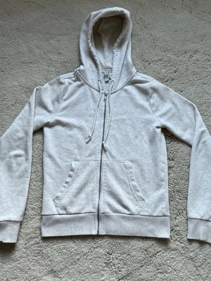 Ljusgrå kofta från H&M - Säljer en ljusgrå kofta från Divided med dragkedja framtill och två fickor. Koftan har huva med snörning och är långärmad. Perfekt för chill dagar och enkel att matcha med jeans eller mjukisbyxor.