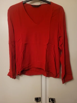 Röd v-ringad blus från Zara Woman - Säljer en snygg röd blus från Zara Woman i storlek S. Blusen har v-ringad hals och långa ärmar, med en lätt och flowy passform. Perfekt för dig som gillar stilrena och färgstarka plagg. Materialet känns mjukt och luftigt mot huden.