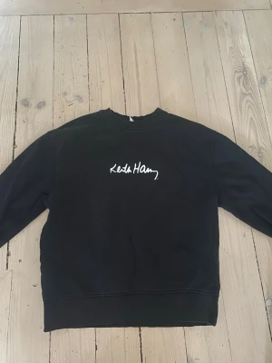 Svart Keith Haring tröja från Zara - Cool svart sweatshirt från Zara x Keith Haring med vit logga framtill och en färgglad skateboard-figur på ryggen. Tröjan har rund hals och långa ärmar, perfekt för dig som gillar streetstyle och konstnärliga prints.