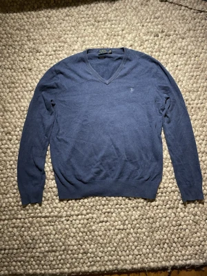 Blå v-ringad tröja från Polo Ralph Lauren - Snygg blå v-ringad tröja från Polo Ralph Lauren i mjuk pima bomull. Tröjan har långa ärmar och diskret logga broderad på bröstet. Perfekt för dig som gillar klassisk och stilren design med skön passform.