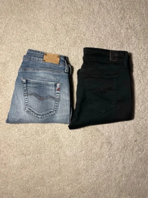 Replay jeans svart & blå, storlek 30 - Två par Replay jeans säljes, ett par svarta och ett par ljusblå. Båda har klassisk femficksdesign och snygga detaljer på bakfickorna. Svarta jeansen har en stilren look medan de blå har kontrastsömmar och tvättad finish. Perfekt för dig som gillar street och casual. Lappen där modellen står är borta!
