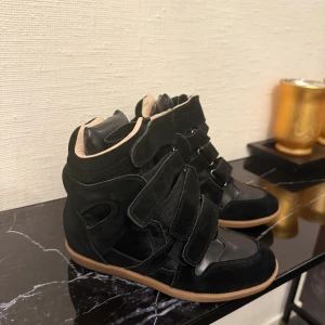 Isabel Marant Skor - Säljer ett par svarta sneakers från Isabel Marant med cool design och högt skaft. Skorna har flera kardborreband, beige insida och gummisula i brunt. Materialet är en mix av mocka och skinn, vilket ger en lyxig känsla. Perfekt för dig som gillar statement-skor. Endast skor medföljs! Kvitto bevis finns på gmailen!