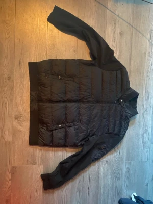 Svart cardigan från Polo Ralph Lauren - Säljer en svart cardigan från Polo Ralph Lauren med broderad logga på bröstet. Jackan har quiltad kropp, släta ärmar, dragkedja framtill och två fickor med knappstängning. Perfekt för kyliga dagar och riktigt snygg till streetwear.