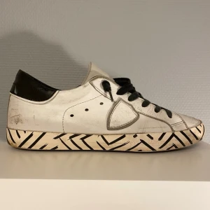 Philippe Model skor - Vita Philippe Model skor med svarta detaljer på sulan. Skorna kommer i stl 40 och är i bra skick, de mesta slitningarna är design. Undersulan är dock lagad med lim eftersom den brast lite vid hälen. Hör av er vid frågor!