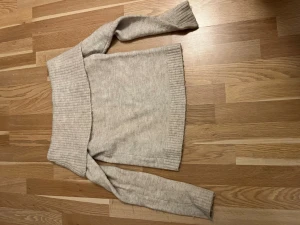 Beige offshoulder stickad tröja - Säljer en beige stickad tröja med bred offshoulder-krage och långa ärmar. Tröjan har ribbade detaljer vid krage, ärmslut och nederkant. Perfekt för dig som gillar en chill och snygg stil under kyliga dagar.