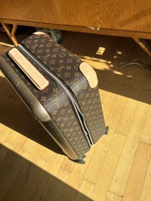 Louis Vuitton resväska monogram brun - Säljer en lyxig resväska från Louis Vuitton i klassiskt monogrammönster. Väskan är brun med beiga detaljer och har hjul för smidig transport. Tillverkad i skinn och syntetmaterial, med dragkedja och flera fack inuti för smart packning.