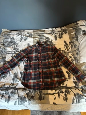 Rutig skjorta från Lee - Säljer en rutig skjorta från Lee i regular fit, storlek M. Skjortan har en klassisk krage, långa ärmar och knappar framtill. Färgerna är mörkblå, röd och beige, och materialet är mjuk bomull. Perfekt för dig som gillar avslappnad stil med lite edge. Skjortan är i mycket bra skick. Har du ytterligare frågor är det bara att höra av sig!