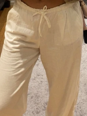Vita linnebyxor med snörning - Säljer ett par vita linnebyxor med avslappnad passform och snörning i midjan. Byxorna har en loose stil och är perfekta för varma dagar. Materialet är linne och färgen är vit, vilket ger en fräsch och chill vibe.
