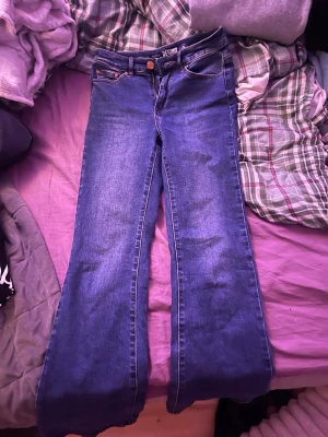 Blå bootcut jeans från Denim 1953 - Säljer ett par snygga blå bootcut jeans från Denim 1953, modell Susan. Jeansen har klassisk femficksdesign, knapp och dragkedja fram samt en schysst tvättad look. Materialet är hållbart denim och passformen är normal. Perfekta för dig som gillar retrovibbar och bekväma jeans.