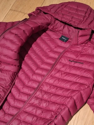 Mörkrosa pufferjacka Peak Performance - Säljer en snygg mörkrosa pufferjacka från Peak Performance med huva och dragkedja. Jackan har quiltad design och är tillverkad i syntetmaterial som håller dig varm under kyliga dagar. Perfekt för dig som vill ha en stilren och funktionell jacka.