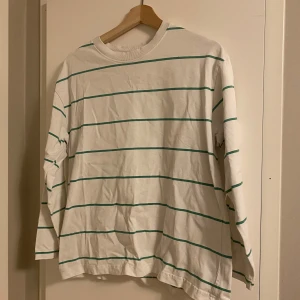 Vit grön randig långärmad tröja Gina Tricot - Vit långärmad tröja från Gina Tricot, basically basics-kollektionen. Tröjan har tunna gröna horisontella ränder och är gjord i mjuk bomull. Perfekt för en chill och enkel stil, passar till jeans eller shorts.