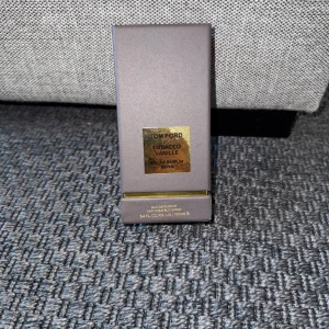 Tom Ford Tobacco Vanille 100ml EdP - Lyxig parfym från Tom Ford, Tobacco Vanille Eau de Parfum i 100 ml flaska. Flaskan är svart och har en elegant, fyrkantig form med guldfärgad etikett. Kommer i en stilren grå ask med gulddetaljer. Doften är kryddig och söt med inslag av tobak och vanilj.