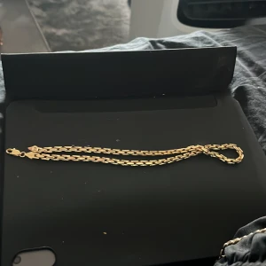 Guldfärgat kedjehalsband - Två Snygga halsband och en snygg påse till i guldfärg med klassisk kedjedesign. Länkarna är platta och breda vilket ger ett coolt och stilrent intryck. Perfekt för dig som vill ha en enkel men ändå iögonfallande accessoar. Lås med karbinhake för extra säkerhet.