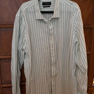 Randig skjorta Clean Cut Copenhagen XXL - Snygg skjorta från Clean Cut Copenhagen i storlek XXL. Ljusgrön och vit med vertikala ränder, klassisk krage och raka knappar framtill. Broderad X-detalj på bröstet. Skjortan är långärmad och har en rak passform, perfekt för en clean och stilren look. Skjortan är knappt använd och i nytt skick. Den kostar 900kr ny.